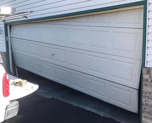 Damaged and bent white steel garage door with panels.