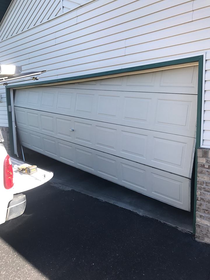 Damaged and bent white steel garage door with panels.