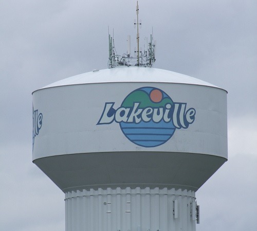 White water tower with blue and green lakeville logo with white lettering with a cloudy background.