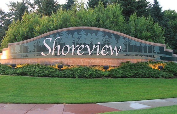 Concrete city of Shoreview sign with a green lawn in the front and bushes infront of the sign with trees in the background.