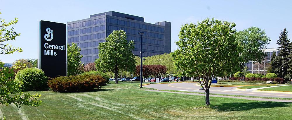 Outside of general mills with a green lawn and trees with shrubbery in the front and the general mills building in the background.